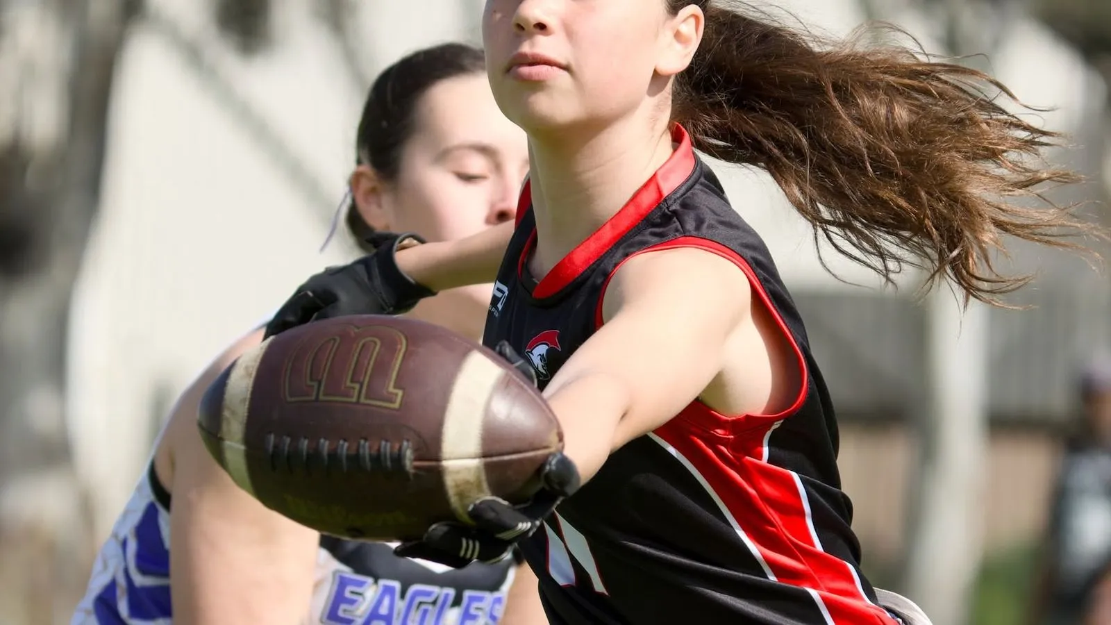 A Spartans flag player stretches out to catch the ball as an Eagles player closes in